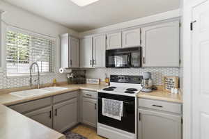 Kitchen with black microwave, range with electric stovetop, a sink, backsplash, and light countertops