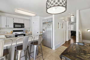 Kitchen featuring stainless steel refrigerator with ice dispenser, electric range, black microwave, a peninsula, and baseboards