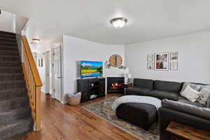 Living room with wood finished floors, stairs, and a lit fireplace