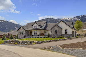 View of front facade with stone siding, a mountain view, a front lawn, board and batten siding, and a porch