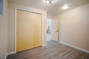 Unfurnished bedroom with a textured ceiling, a closet, baseboards, and wood finished floors