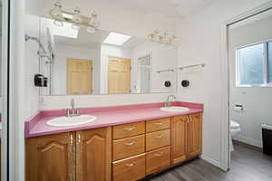 Bathroom featuring toilet, a skylight, double vanity, and a sink