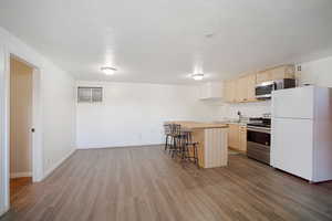 Kitchen featuring a breakfast bar area, light brown cabinetry, appliances with stainless steel finishes, decorative backsplash, and dark wood-style floors