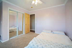 Bedroom featuring a ceiling fan, a closet, baseboards, crown molding, and light colored carpet