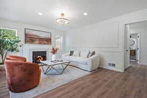 Living area featuring wood finished floors, plenty of natural light, a tile fireplace, moldings, and a chandelier