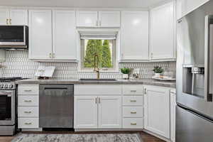 Kitchen with stainless steel appliances, a Blanco single bowl sink, white cabinetry, and decorative backsplash