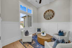 Sitting room with beamed ceiling, a decorative wall, a ceiling fan, wood finished floors, and wainscoting
