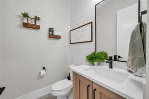 Bathroom with toilet, vanity, baseboards, and wooden walls