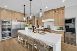 Kitchen featuring built in appliances, exhaust hood, a kitchen bar, tasteful backsplash, and a sink