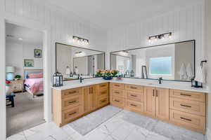 Ensuite bathroom featuring marble look tiles, double vanity, crown molding, and wooden walls
