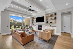 Living area featuring ceiling fan, light wood-style flooring, a glass covered fireplace, baseboards, and beamed ceiling