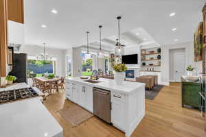 Kitchen featuring stainless steel dishwasher, a sink, a glass covered fireplace, light wood finished floors, and light countertops