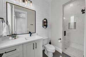 Bathroom featuring tile patterned floors, a shower stall, toilet, vanity, and wood walls