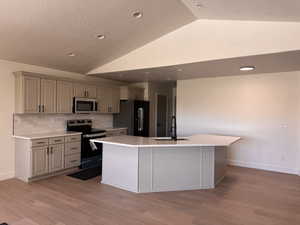 Kitchen featuring stainless steel appliances, vaulted ceiling, a sink, light countertops, and decorative backsplash
