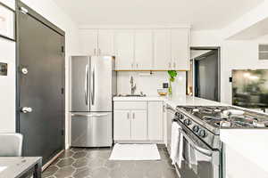 Kitchen featuring freestanding refrigerator, gas stove, a sink, quartz countertops, and off white cabinetry