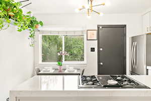 Kitchen featuring freestanding refrigerator, gas stovetop, a chandelier, white cabinetry, and quartz counters