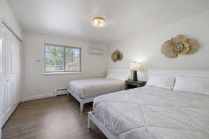 Bedroom featuring an AC wall unit, wood finished floors, baseboard heating, a closet, and baseboards
