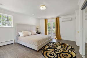 Bedroom with a wall mounted air conditioner, access to exterior, ornamental molding, wood finished floors, and a baseboard heating unit