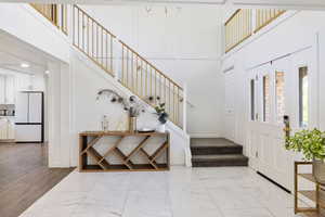 Entryway with light marble finish floors, stairway, and a high ceiling
