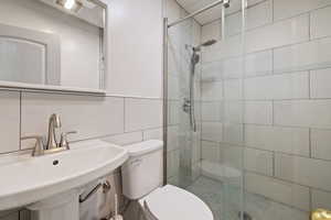 Full bathroom with a sink, tile walls, toilet, and a stall shower