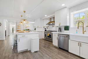 Kitchen featuring stainless steel appliances, wall chimney exhaust hood, decorative backsplash, white cabinetry, and recessed lighting