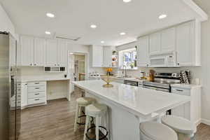 Kitchen featuring open shelves, stainless steel appliances, a breakfast bar area, and white cabinetry