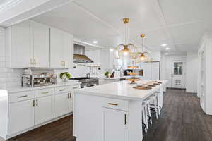 Kitchen with decorative backsplash, white cabinetry, and wall chimney range hood