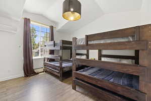 Bedroom featuring vaulted ceiling, wood finished floors, baseboard heating, an AC wall unit, and baseboards