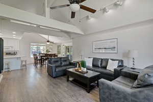 Living area with wood finished floors, baseboards, high vaulted ceiling, rail lighting, and a ceiling fan