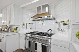 Kitchen featuring backsplash, range with two ovens, light countertops, white cabinets, and wall chimney exhaust hood