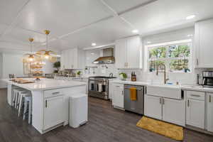 Kitchen featuring stainless steel appliances, wall chimney exhaust hood, a sink, tasteful backsplash, and coffered ceiling