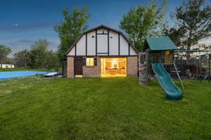 Back of property at dusk with a playground, a yard, brick siding, and an outbuilding