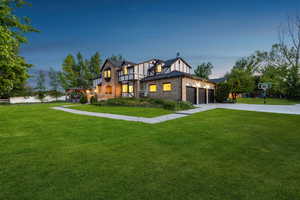 Tudor house with a front yard, brick siding, a garage, and driveway