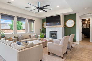 Living room with a ceiling fan, light wood finished floors, baseboards, a fireplace, and arched walkways