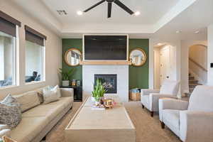 Living room with carpet, a ceiling fan, arched walkways, a glass covered fireplace, and stairs