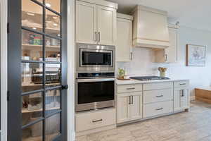 Kitchen with built in appliances, custom exhaust hood, tasteful backsplash, light countertops, and white cabinetry