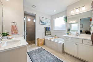 Full bathroom with tile patterned floors, two vanities, a shower stall, and a garden tub