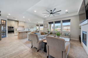 Living area with recessed lighting, a ceiling fan, a glass covered fireplace, baseboards, and a tray ceiling