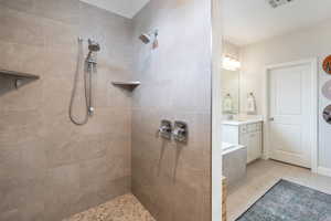 Bathroom featuring tiled shower, vanity, and tile patterned flooring