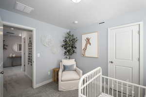 Carpeted bedroom with a crib, baseboards, and a textured ceiling