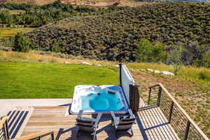 Wooden terrace featuring an outdoor hot tub and a lawn
