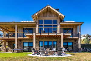 Rear view of property with a balcony, stone siding, a standing seam roof, a patio area, and board and batten siding