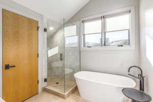 Full bath with a shower stall, a freestanding bath, vaulted ceiling, and tile patterned floors