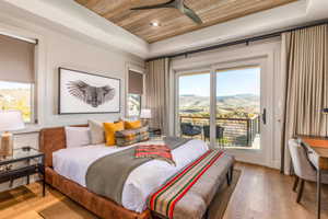 Bedroom featuring a tray ceiling, wood ceiling, access to outside, multiple windows, and light wood-type flooring