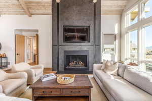 Living room with wood ceiling, beamed ceiling, a large fireplace, and wood finished floors