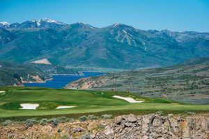 View of mountain backdrop featuring a golf course and a nearby body of water