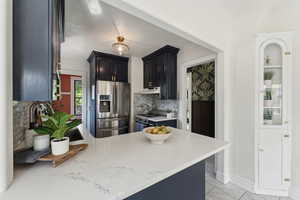 Kitchen featuring a sink, a peninsula, decorative backsplash, stainless steel fridge, and range with gas stovetop