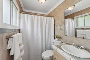 Bathroom featuring tile walls, toilet, a shower with shower curtain, vanity, and crown molding