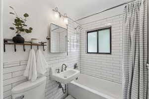 Bathroom with shower / bath combo with shower curtain, toilet, tile walls, and a sink