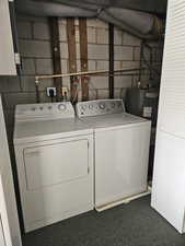Washroom featuring concrete block wall, washing machine and dryer, dark colored carpet, and water heater